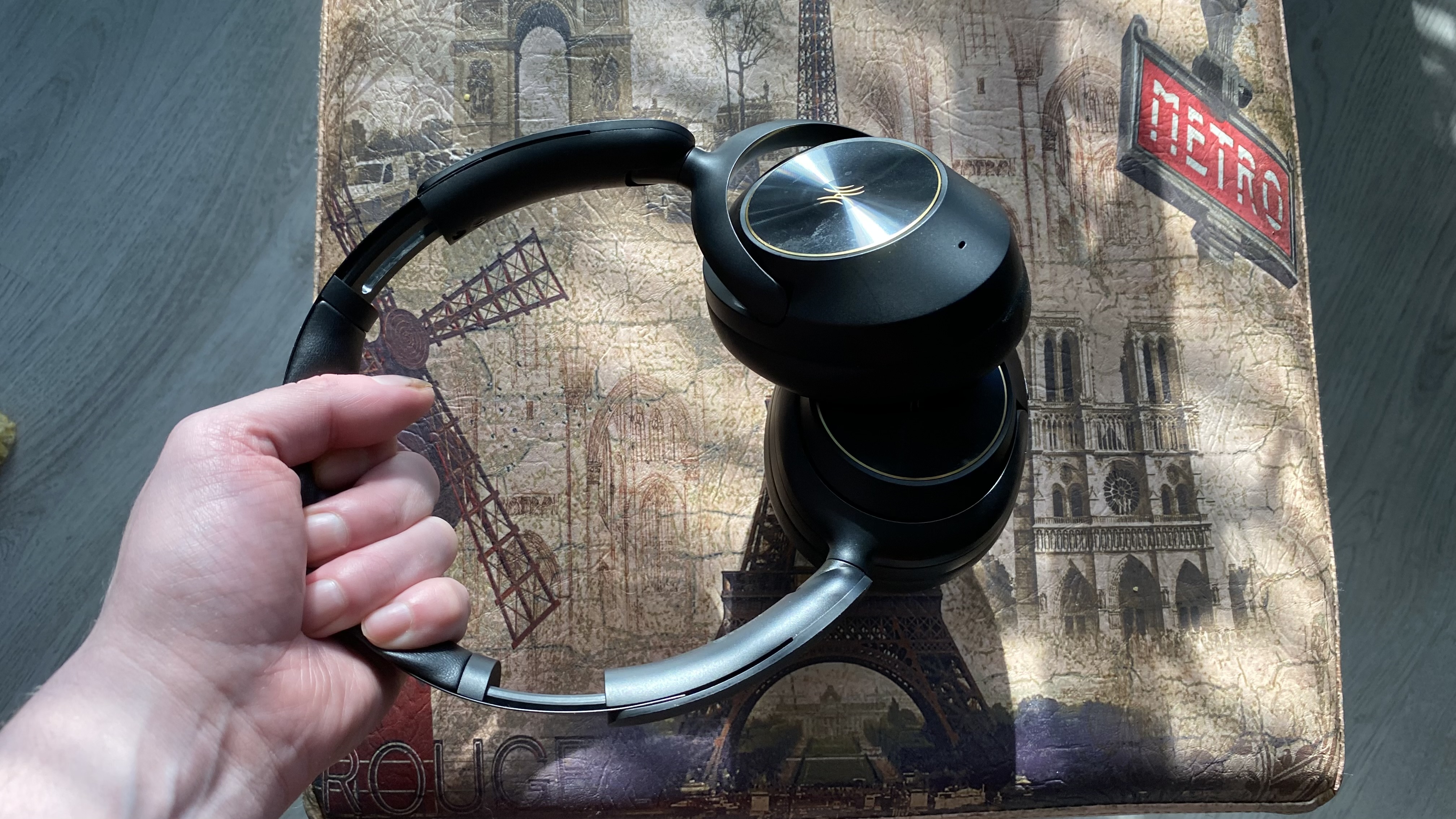 OneOdio Focus A6 over-ear headphones held by the head strap over a Parisian stool