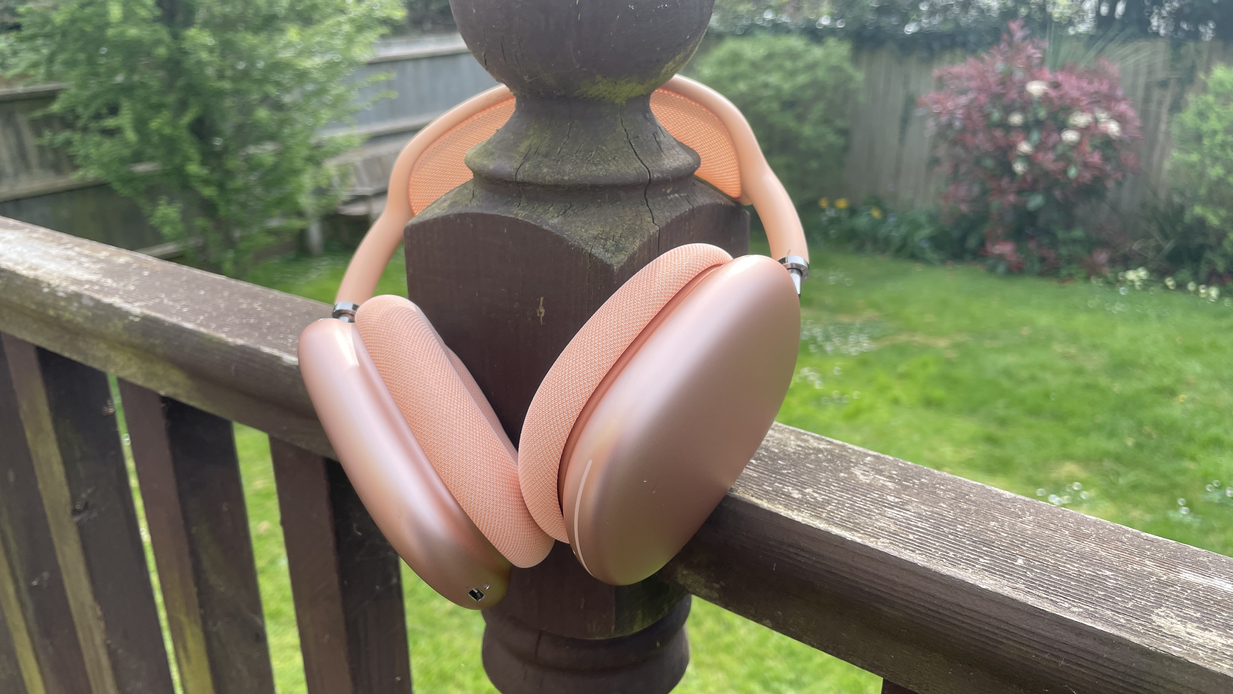 Apple AirPods Max 2 in orange with AirPods Max just visible in purple, outside in a garden on a bench, held in hand