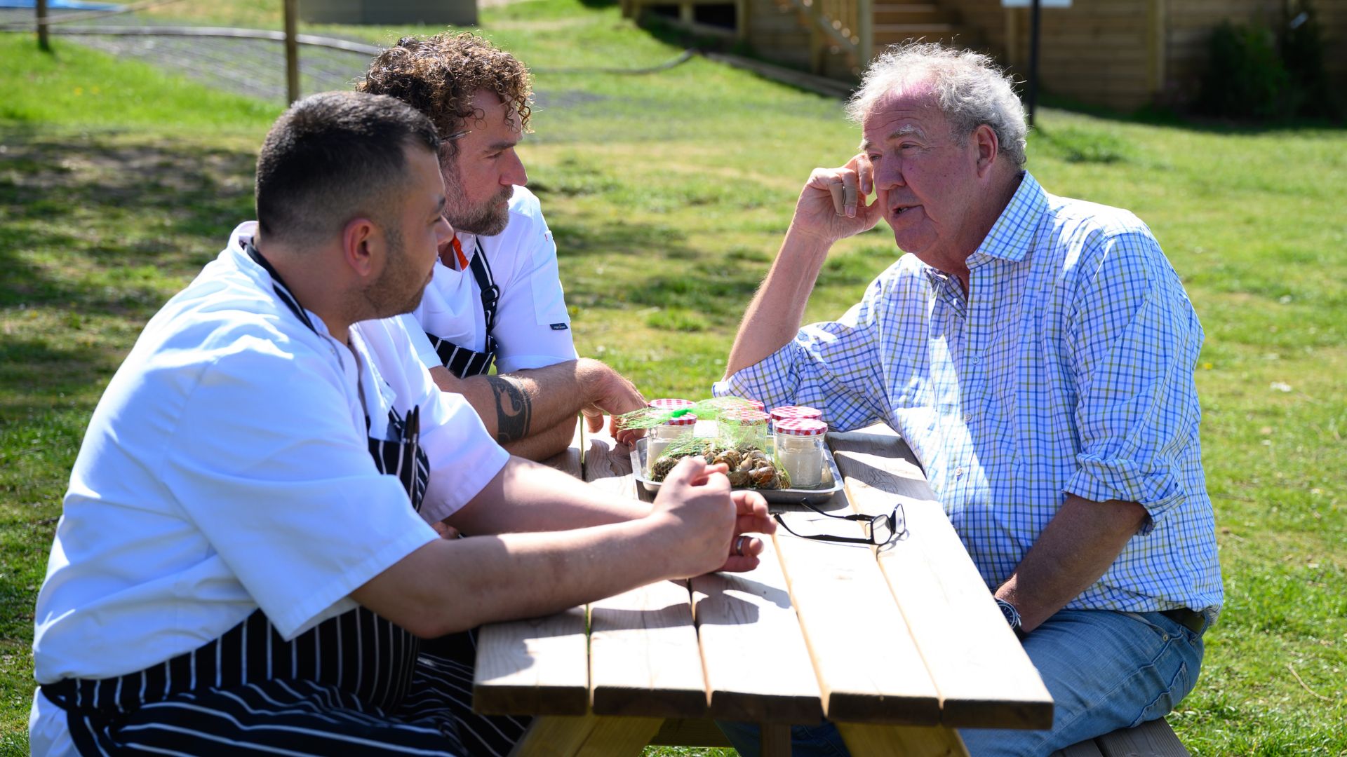 Jeremy is talking to two chefs over a picnic table