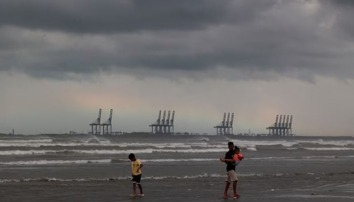 Children play with the rainbow and rain clouds in the background at Clifton Beach in Karachi, August 30, 2024. — Reuters