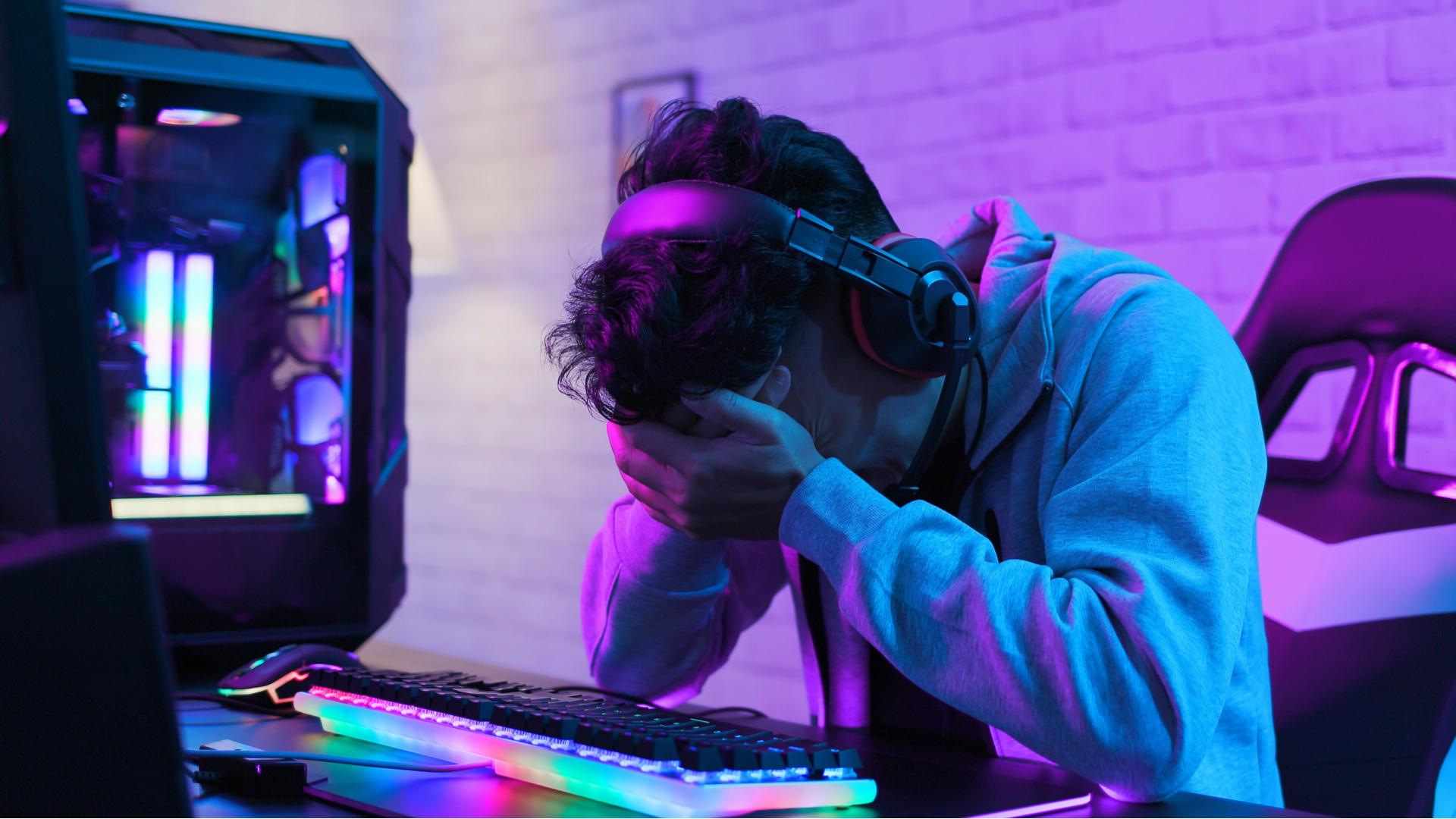 A sad person with his head in his hands sat at a gaming PC