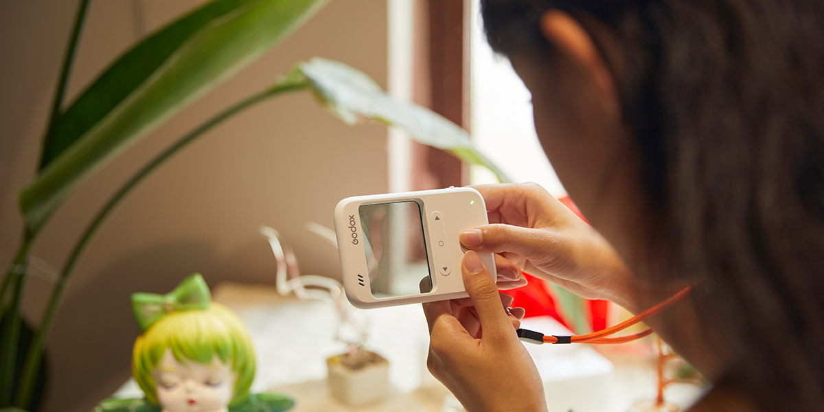 Woman holds Godox C100 transparent window camera and uses it to take a photograph of a plastic doll