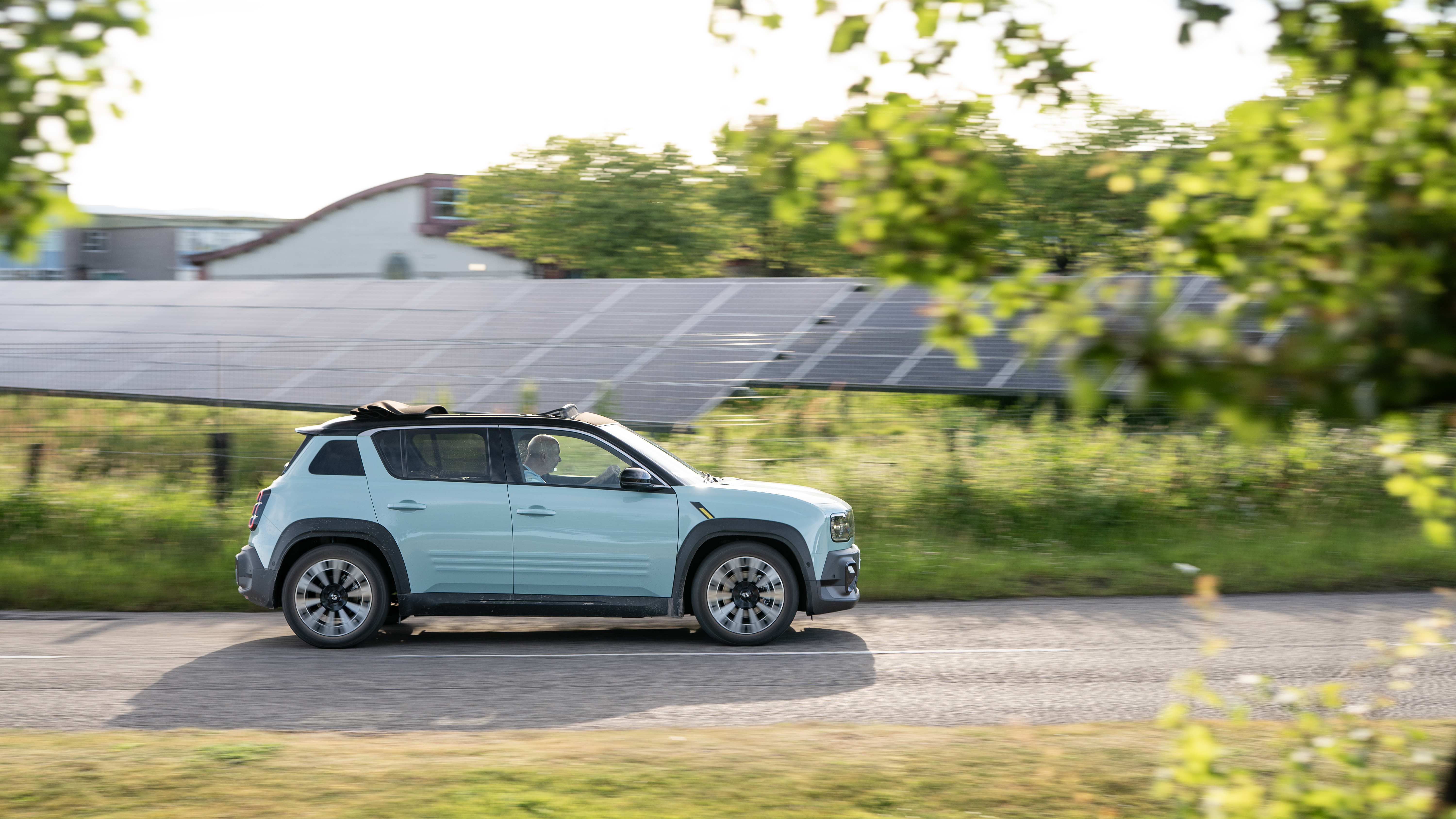 An electric car drives in front of a solar farm