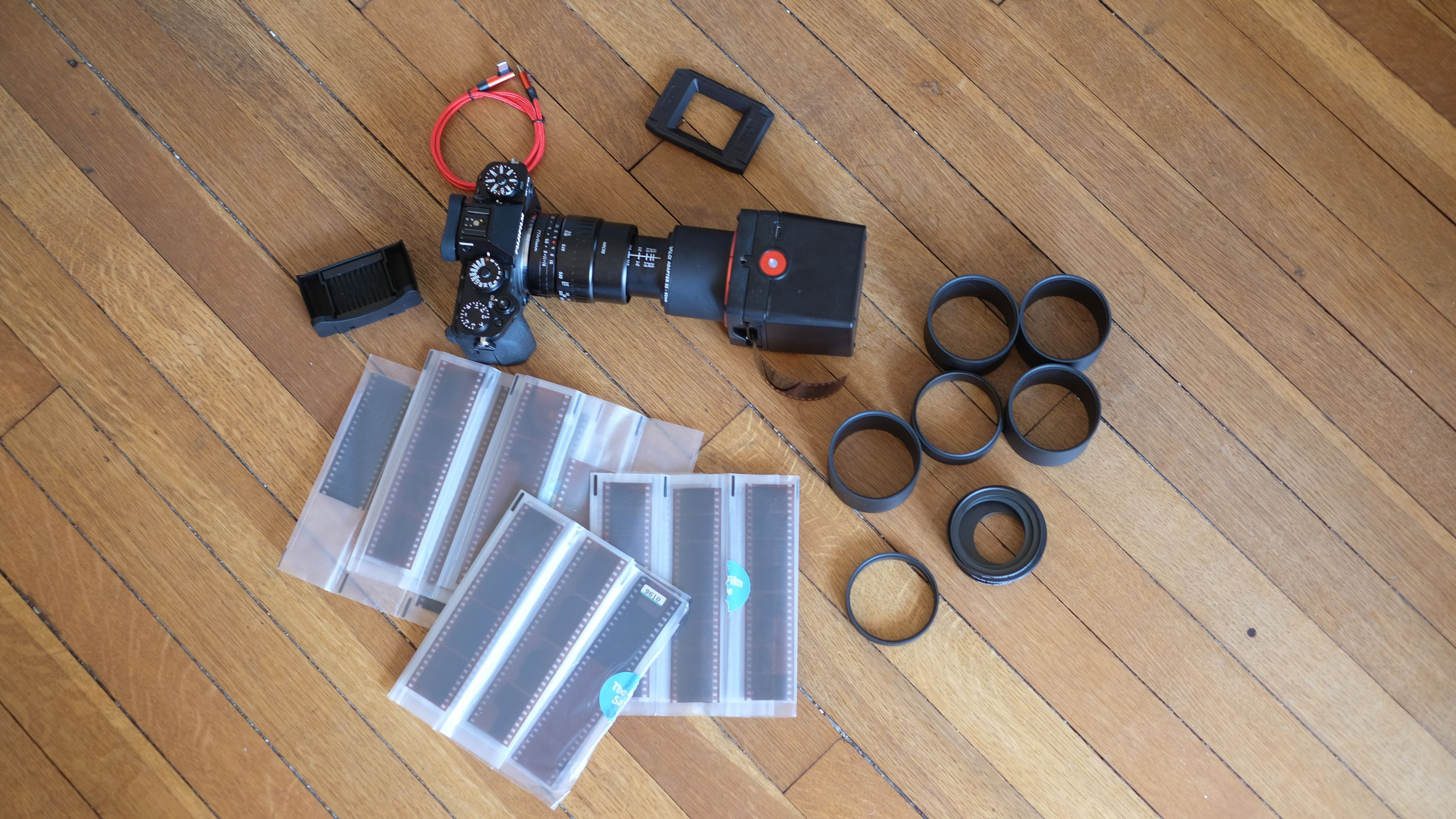 Photograph of the Valoi Easy35 V2 film scanner set laid out on the floor, including camera, scanner, extension tube, holder, dust brush, USB cable and film negatives