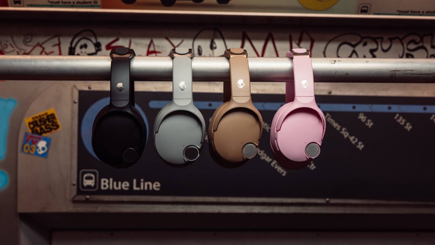 Four different color models of the Skullcandy Crusher 1080, hung on a bar in a subway.