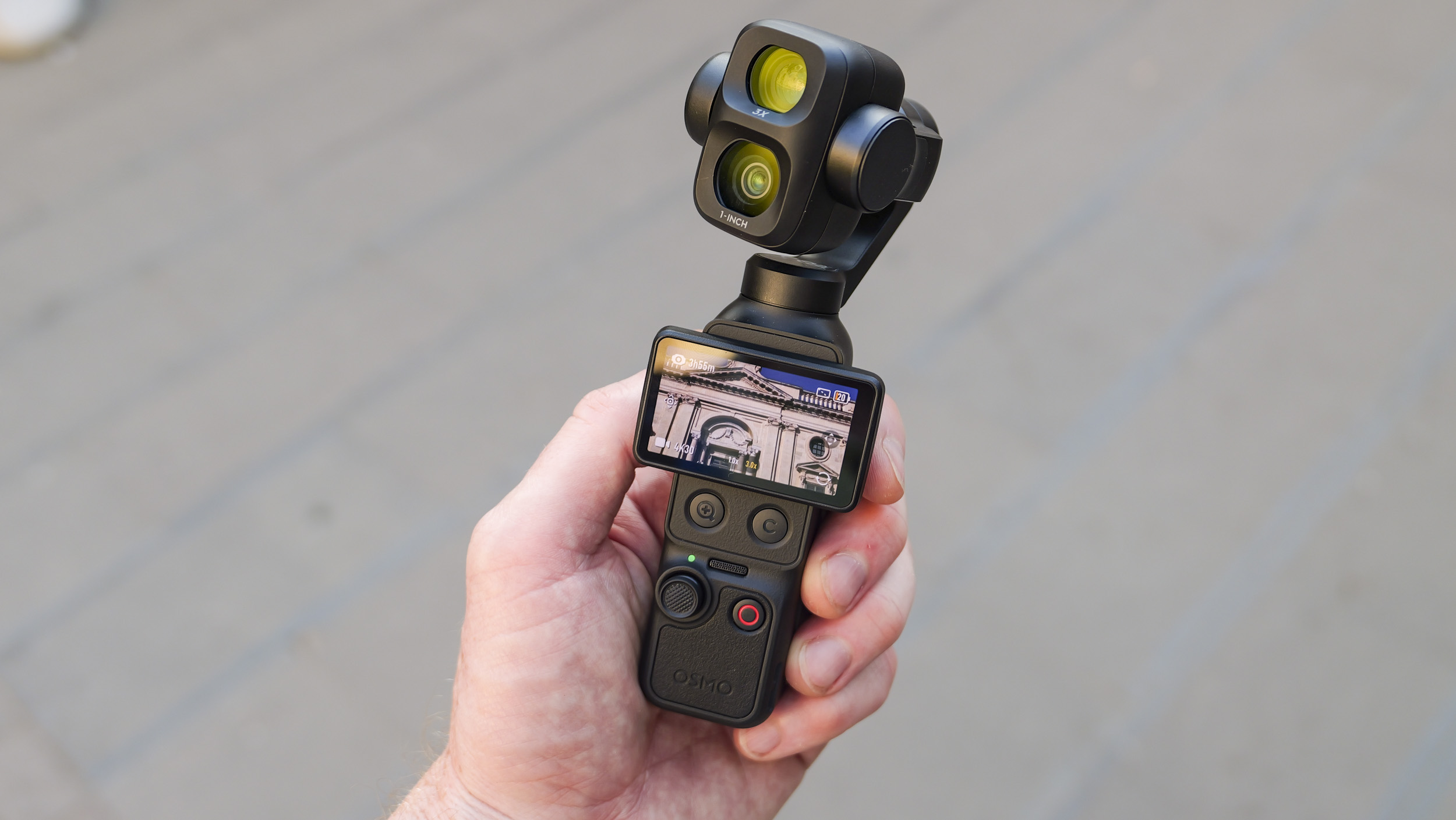 DJI Osmo Pocket 4P vlogging camera in a person's hand in a city street, screen rotated horizontally