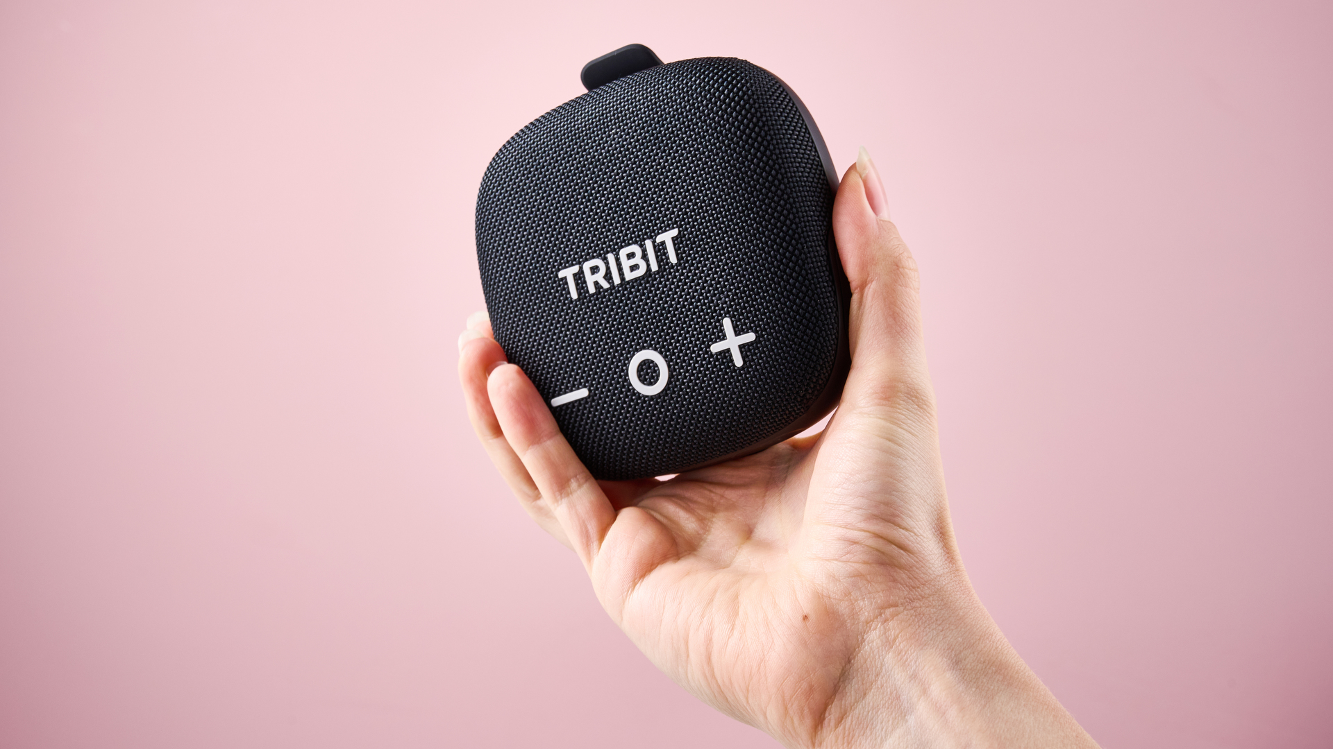 A woman's hand holds up the Tribit Stormbox Micro 3 in front of a pink background.